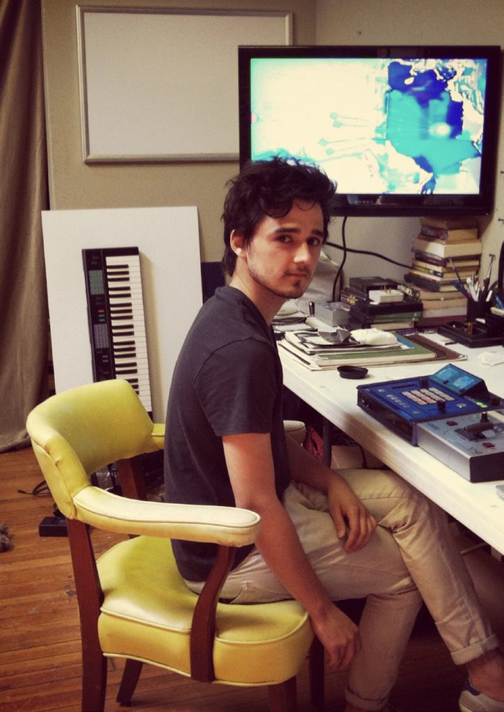 Artist looks at the camera as he sits in front of his desk.
